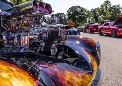 Close-up of a custom car with a flame paint job at a car show, surrounded by other colorful cars.