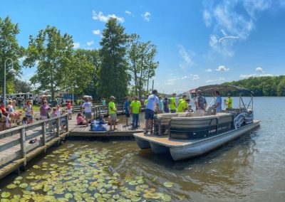 A group of people gather on a dock as a pontoon boat arrives on a sunny lake day.