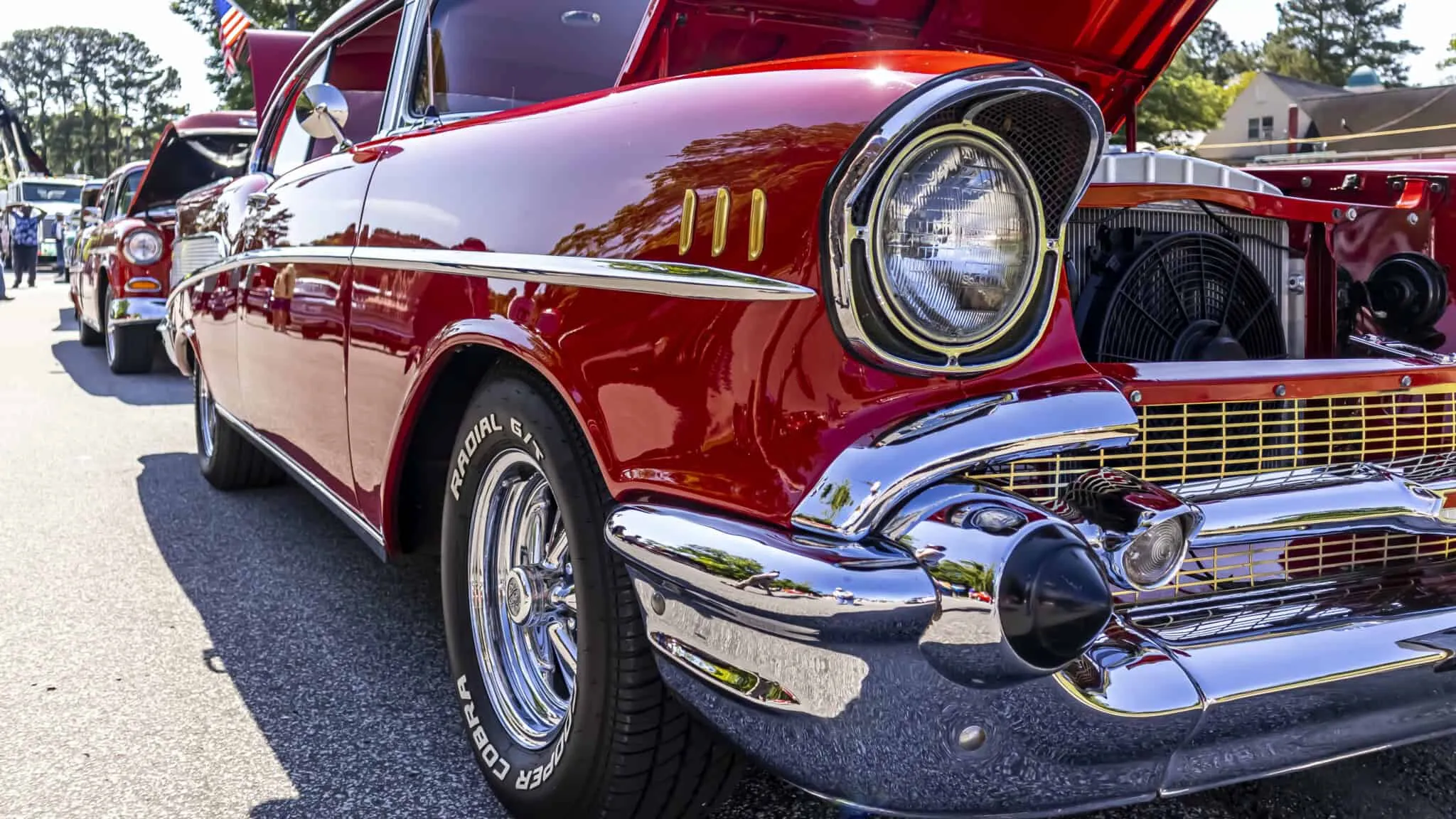 Close-up of a shiny red vintage car with hood open, showcasing chrome details at a car show.