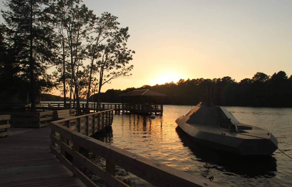 A dock with a wooden boardwalk and a docked submarine at sunset over a calm lake.