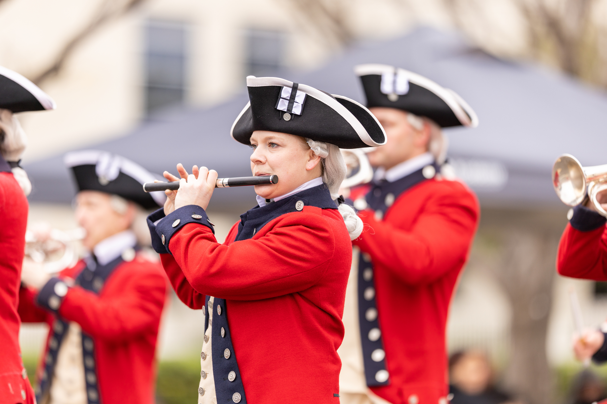 People in historical uniforms play flutes and trumpets during an outdoor event or parade.