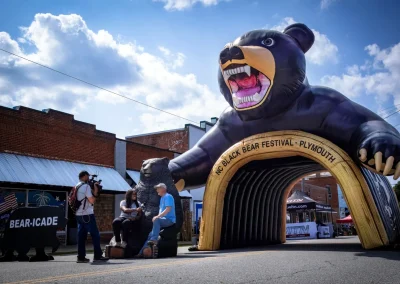 A giant inflatable black bear archway at the NC Black Bear Festival in Plymouth, with people nearby.