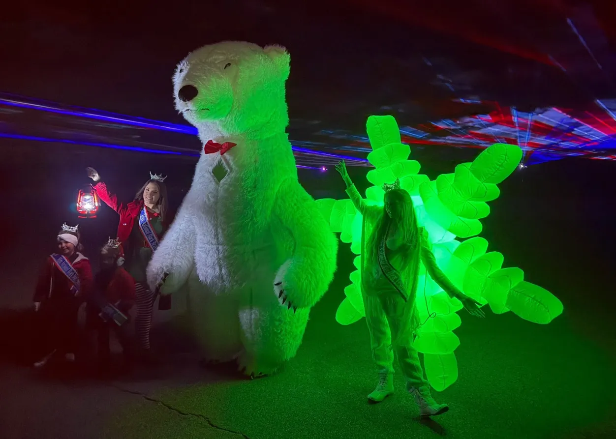 People in costumes stand with a giant polar bear and a person in a glowing green suit under colorful lights.