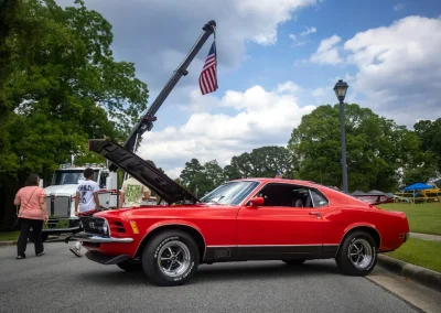 A red classic car with its hood open is parked near a crane holding an American flag.