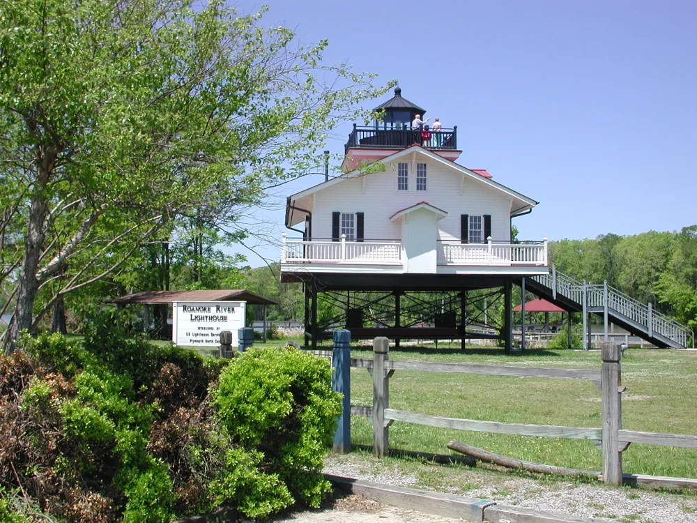 maritime-museum-1 A white river lighthouse on stilts surrounded by greenery, with a sign and wooden fence in the foreground.